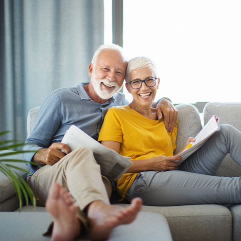 Ein älteres Paar schaut sich auf dem Sofa die Unterlagen zur fondsgebundenen Rentenversicherung an.
